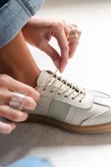 Zapatilla de cuero color crudo con detalle de una franja lateral en verde agua y cordones color beige.