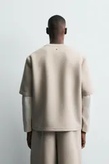 Sudadera de corte oversize confeccionada en tejido técnico de algodón con elasticidad, cuello redondo y manga corta. Presenta una tacha metálica decorativa en la parte posterior.