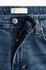 Jean de tiro alto con corte acampanado desde la rodilla, confeccionado en denim con leve elasticidad. Presenta diseño clásico de cinco bolsillos, cierre frontal con botón y acabado en tono azul medio.