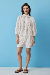Camisa de broderie color blanco, con cuello clásico, mangas abullonadas y cierre frontal oculto.