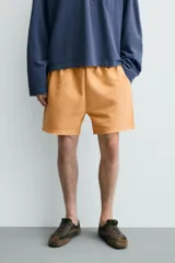 Bermuda de corte relajado confeccionada en tejido de algodón con interior de rizo. Presenta cintura elástica con cordón ajustable, bolsillos laterales, un bolsillo trasero de plastrón y bajo con acabado irregular con efecto lavado.