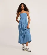 Vestido midi de jean azul con breteles finos, escote recto y falda con volados escalonados. Presenta un ajuste elástico en el busto y diseño holgado.