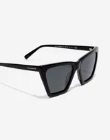 Lentes de sol Hawkers unisex, modelo Flush, con montura geométrica negra y lentes polarizadas oscuras.