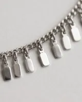 Tobillera de acero con cadena eslabonada y pequeños dijes colgantes rectangulares.