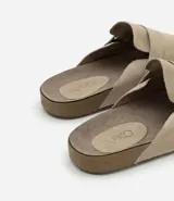 Ojota mule color beige confeccionada en cuero, con tira ancha y hebilla metálica.