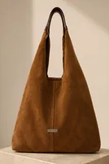 Bolso tipo hobo grande confeccionado en cuero vacuno color marrón, con costura central vertical y placa metálica con el logo de la marca Pecarí.