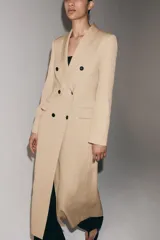 Abrigo largo de corte recto y diseño fluido, confeccionado en tejido con mezcla de lino. Presenta cuello con solapas, cierre frontal cruzado con botones en contraste y bolsillos laterales con solapa.