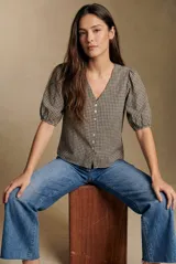 Blusa de algodón con estampado de cuadros vichy en tonos negro y blanco. Presenta escote en V, cierre frontal con botones y mangas cortas abullonadas con terminación elástica.