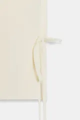 Chaleco color crema de punto, con escote en pico y sin mangas. Cierre cruzado frontal con lazada lateral.