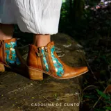 Botas de caña corta de cuero marrón con detalles pintados a mano en tonos turquesa y dorado, puntera fina, taco cuadrado de madera y doble cierre lateral con tiradores metálicos.