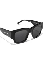 Gafas de sol unisex Hawkers X Augusto Fernandez, de acetato negro con lentes polarizadas negras y logo de la marca en la patilla.