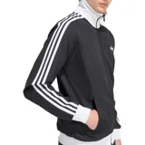 Campera deportiva Adidas modelo Beckenbauer, color negro con cuello alto, puños y cintura en color blanco. Presenta las icónicas tres tiras blancas en las mangas y el logo del trifolio bordado en el pecho.