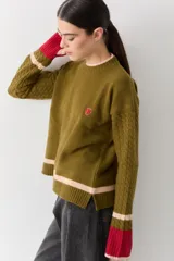Buzo de lana con cuello redondo, mangas largas con diseño de ochos y puños con abertura para el pulgar. Presenta un diseño tricolor en bloques con franjas en tonos bordó, mostaza y beige.