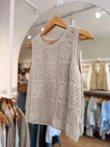 Musculosa tejida de color natural, con diseño calado de motivos geométricos y florales, escote redondo y silueta sin mangas.