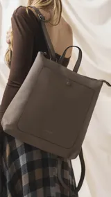 Mochila de diseño moderno y funcional, confeccionada en símil cuero con textura granulada. Cuenta con un bolsillo frontal con broche, cierre principal superior, manija superior y correas ajustables. Incluye logo de la marca grabado en el frente.