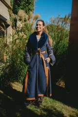 Abrigo largo de diseño envolvente tipo bata, confeccionado en una combinación de tweed azul marino y secciones capitonadas. Presenta solapas amplias con detalle de corderito azul, cinturón de cuero marrón para ajustar a la cintura y vivos de cuero en los bordes. Incluye mangas largas con puños amplios y detalles artesanales.