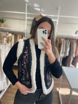 Chaleco negro con bordados florales en tonos celeste, azul, blanco y mostaza, con forro de corderito color crema.