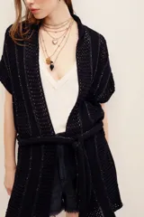 Chaleco largo de punto negro con diseño abierto y cinturón ajustable en la misma tela. Presenta detalles de hilos metalizados y tramas caladas.
