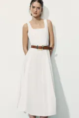 Vestido midi de color blanco con escote cuadrado y tirantes finos. Presenta un diseño acampanado con pliegues y un cinturón de cuero sintético en color tostado con hebilla metálica dorada.