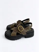 Sandalias de plataforma con suela track negra y capellada de cuero con textura simil cocodrilo en color verde militar. Cuentan con tiras cruzadas y una hebilla metálica grande en tono bronce.