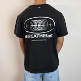 Remera negra de corte regular con estampa gráfica en la espalda que incluye un diseño circular abstracto y el texto BREATHEfast.