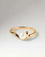 Anillo de oro con diseño envolvente y una perla central incrustada.