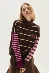 Sweater de tejido de punto con cuello polera baja, cuerpo marrón con rayas horizontales amarillas y mangas largas a rayas verticales en tonos rosado y morado. Presenta un bordado floral en el pecho.