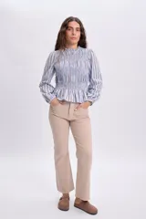 Blusa celeste a rayas marrones y blancas, con diseño de punto smock en el pecho y mangas largas abullonadas con puños elásticos.