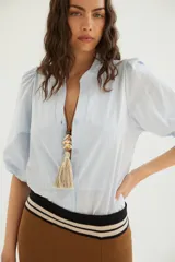 Camisa de algodón celeste con cuello mao, pechera con botones ocultos y mangas abullonadas con puños elásticos.