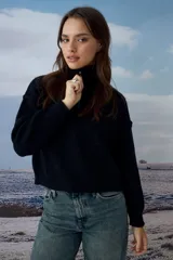 Sweater tejido de punto color negro, con cuello alto y cierre frontal parcial. Presenta mangas largas con hombros caídos y un corte cropped.