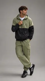 Campera con capucha de diseño bicolor, combinando verde oliva en la parte superior y negro en la inferior. Cuenta con cierre frontal completo, puños elásticos y un pequeño logo bordado en el pecho.