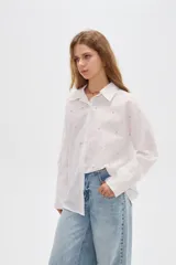 Camisa de algodón blanca, de corte oversize, manga larga y cuello camisero, decorada con apliques de strass y bordados sutiles en la parte delantera.