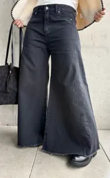 Jean de corte oxford y tiro medio, color negro lavado. Presenta diseño de pierna ancha con costuras verticales decorativas y ruedo deshilachado.