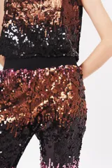 Babucha de poliéster con lentejuelas en degradado de colores: negro, dorado y rosado. Tiene forro interior y puños elásticos en los tobillos.