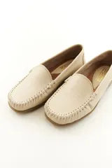 Mocasines de cuero vacuno color beige con acabado mate, costuras visibles artesanales en el empeine y suela de perfil bajo.