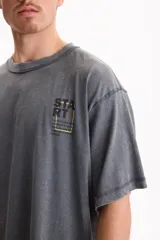Remera oversize gris de manga corta con efecto lavado acid wash y estampa pequeña en el pecho con la palabra 'START' dentro de un recuadro amarillo.