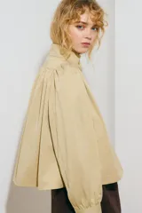Campera corta de sarga color beige, con cuello alto, cierre frontal de botones, mangas largas abullonadas con puños ajustados y bolsillos laterales ribeteados.