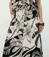 Pollera larga (midi) de corte evasé, con cintura elástica y lazo. Presenta un estampado grande en blanco y negro de motivos tropicales como hojas de palmera y flores.