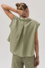 Blusa verde militar sin mangas, confeccionada en lino, con cuello camisero, cierre frontal con botones y corte holgado.