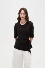 Remera negra de manga corta, con cuello redondo y diseño holgado con detalle de lazo para anudar en la cintura.