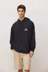 Hoodie negro de corte holgado con capucha ajustable mediante cordones, bolsillo frontal tipo canguro y logo bordado en color blanco en el pecho.