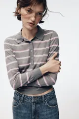Polo de punto fino confeccionado en lana, con diseño de rayas horizontales en tonos gris, blanco y rosado. Presenta cuello polo, manga larga y cierre frontal con botones.