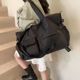 Bolso deportivo multifunción color negro, con diseño liso, compartimento principal con cierre, bolsillo frontal con solapa y bolsillo frontal con cierre. Cuenta con doble asa de mano y correa de hombro ajustable y extraíble. Incluye detalle de logo circular en la parte inferior.
