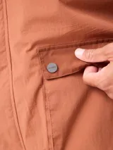 Campera impermeable Rusty con capucha, confeccionada en nylon. Presenta cierre frontal con botones a presión, bolsillos delanteros con solapa y puños elásticos.