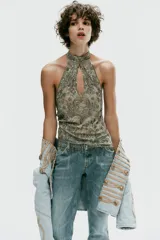 Top halter confeccionado en mezcla de poliamida, color verde militar, con diseño cut-out en el escote, espalda descubierta y aplicaciones de abalorios y lentejuelas brillantes. Presenta bajo recto con flecos colgantes de cuentas y cierre posterior con botones en el cuello.