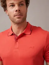 Chomba de piqué color ladrillo, con cuello polo de dos botones y logo bordado en el pecho. Presenta ribetes en cuello y mangas.