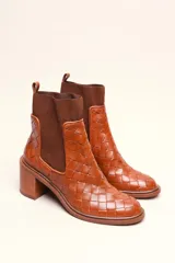 Bota tipo botineta de cuero negro con diseño trenzado artesanal en toda la capellada. Presenta paneles laterales elásticos, taco cuadrado de altura media y tirador en la parte superior trasera.