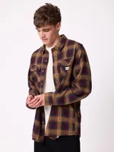 Camisa de franela Rusty de manga larga, con diseño a cuadros en tonos marrones y rojizos. Presenta cuello clásico, cierre frontal con botones y dos bolsillos en el pecho con solapa.