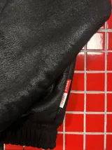 Campera de cuero sintético negro con diseño tipo bomber, cuello camisero y puños y ruedo elásticos. Presenta un bordado grande en la espalda con tipografía cursiva en color blanco.
