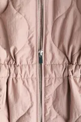 Campera acolchada de nylon guateado en color rosado, con cuello redondo, cierre frontal y cordón ajustable en la cintura con tiras colgantes. Presenta diseño acolchado con patrón de rombos, mangas largas y hombros caídos.